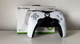 White and black Xbox-branded controller in front of its weight box with green trim.